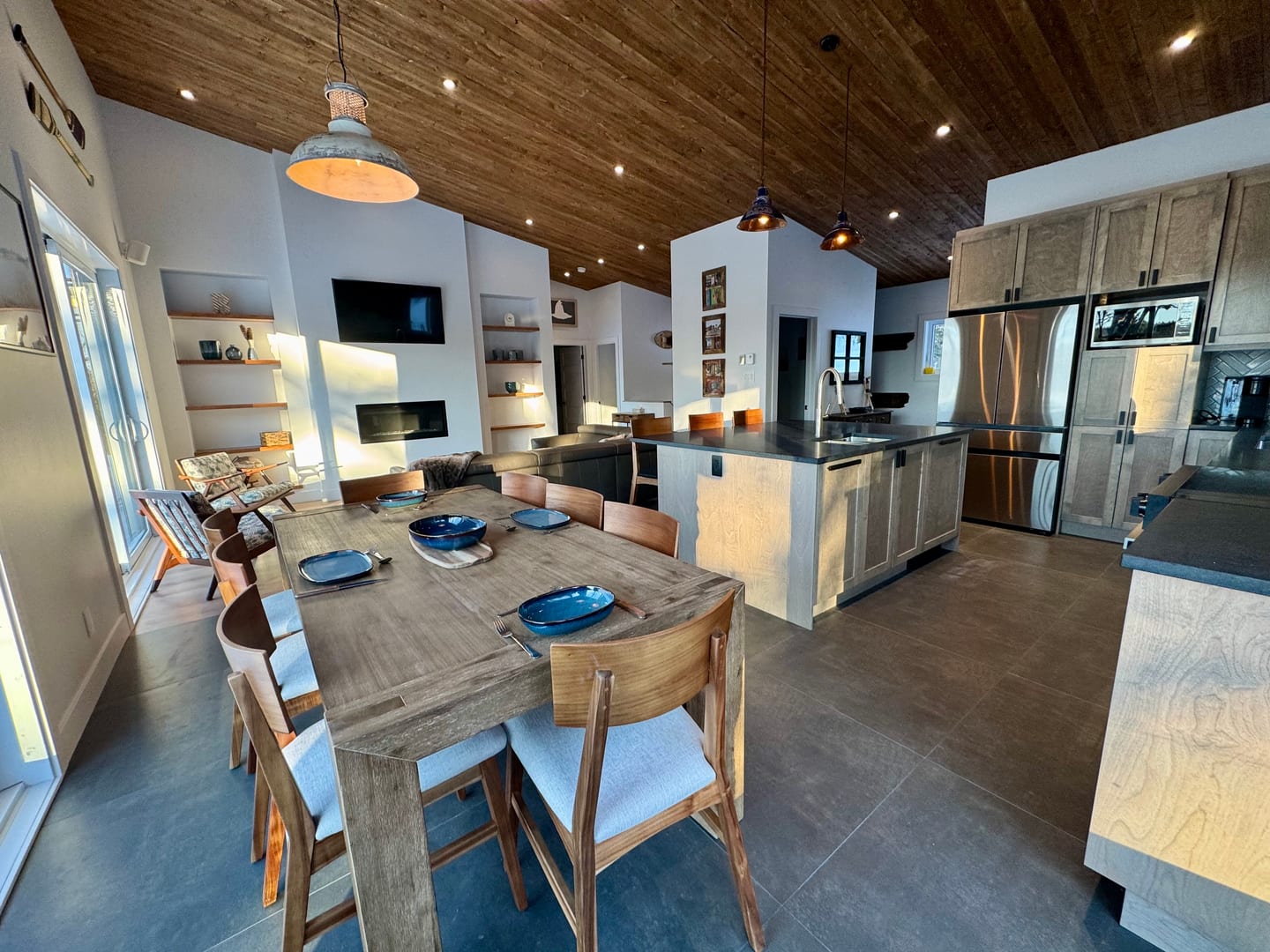 Salle à manger avec longue table, cuisine en îlot et plafond bois